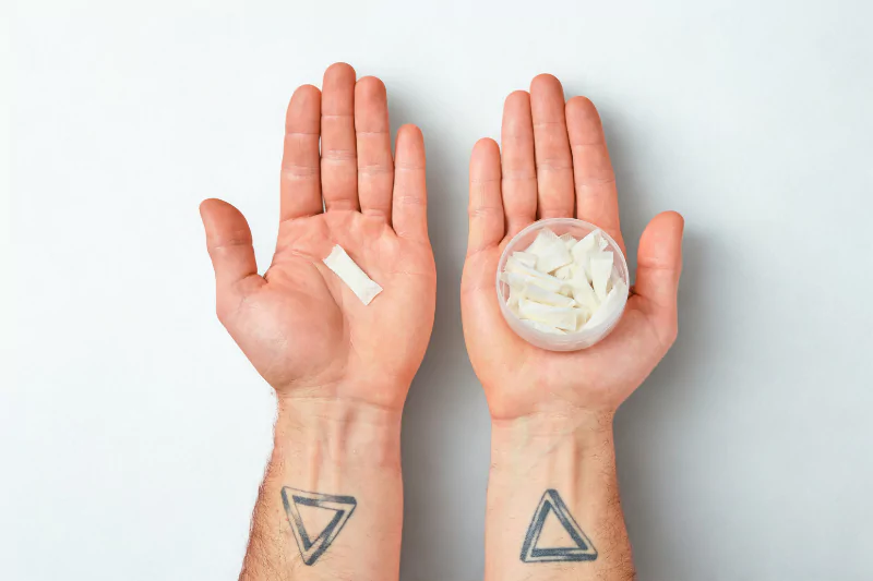 Tattooed hands holding a can of nicotine pouches and a can of snus – Thailand snus comparison
